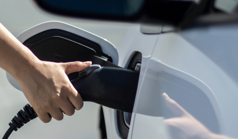 Nahaufnahme eines E-Autos beim Ladevorgang an einer Ladesäule – eine Hand steckt das Ladekabel in den Ladeanschluss des Fahrzeugs. Symbolbild für moderne E-Mobilität und Ladeinfrastruktur an der Tankstelle.