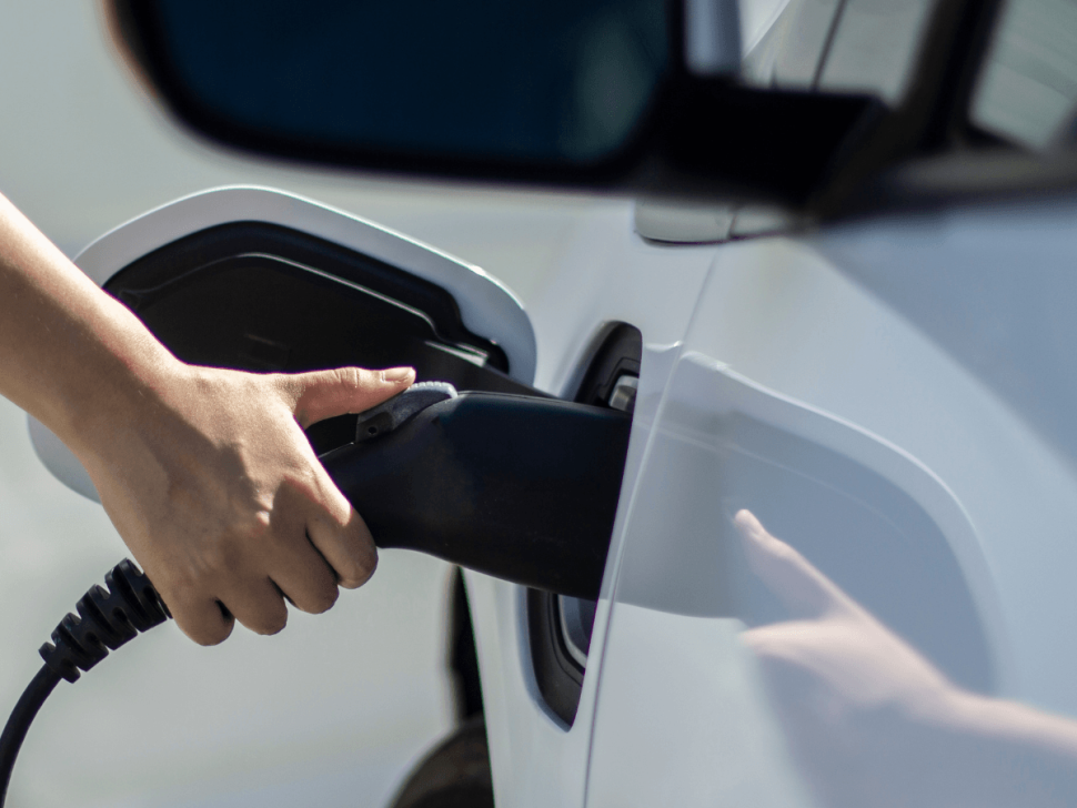 Nahaufnahme eines E-Autos beim Ladevorgang an einer Ladesäule – eine Hand steckt das Ladekabel in den Ladeanschluss des Fahrzeugs. Symbolbild für moderne E-Mobilität und Ladeinfrastruktur an der Tankstelle.