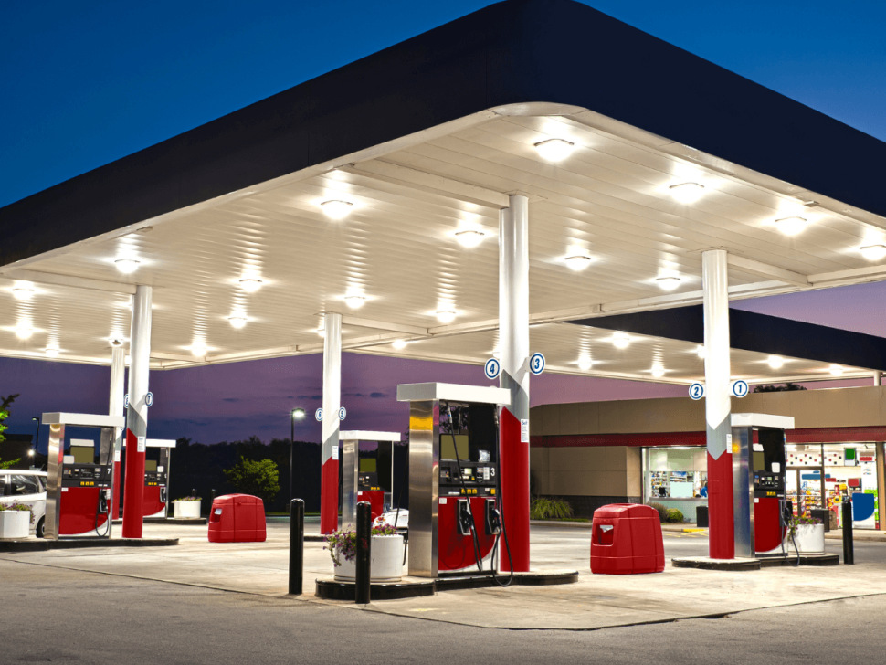 Moderne, beleuchtete Tankstelle in der Dämmerung mit mehreren Zapfsäulen und überdachter Fahrbahn – Symbolbild für zeitgemäßen Tankstellenbetrieb und 24/7-Verfügbarkeit.