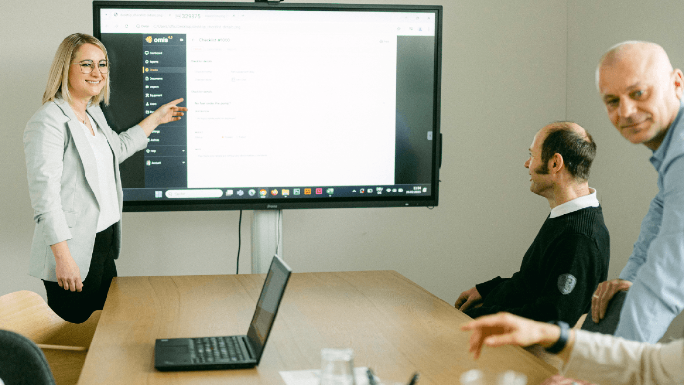Mitarbeiterinnen und Mitarbeiter von omis bei einer Software-Präsentation im Meetingraum – eine Kollegin erklärt die Benutzeroberfläche des omis Tools auf einem großen Bildschirm.