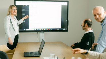 Mitarbeiterinnen und Mitarbeiter von omis bei einer Software-Präsentation im Meetingraum – eine Kollegin erklärt die Benutzeroberfläche des omis Tools auf einem großen Bildschirm.