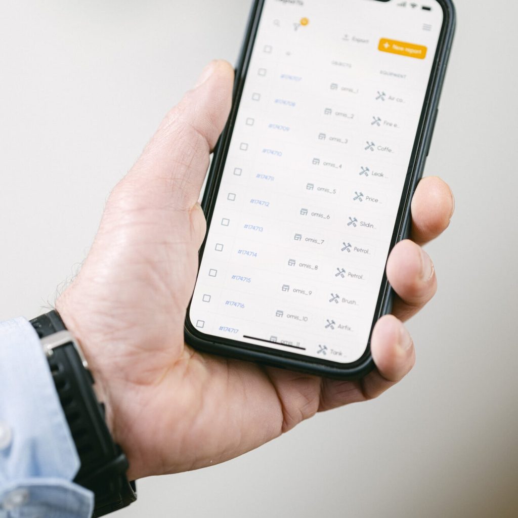 Hand hält Smartphone mit der omis App, die eine Liste von Reports anzeigt – mobile Nutzung von omis.