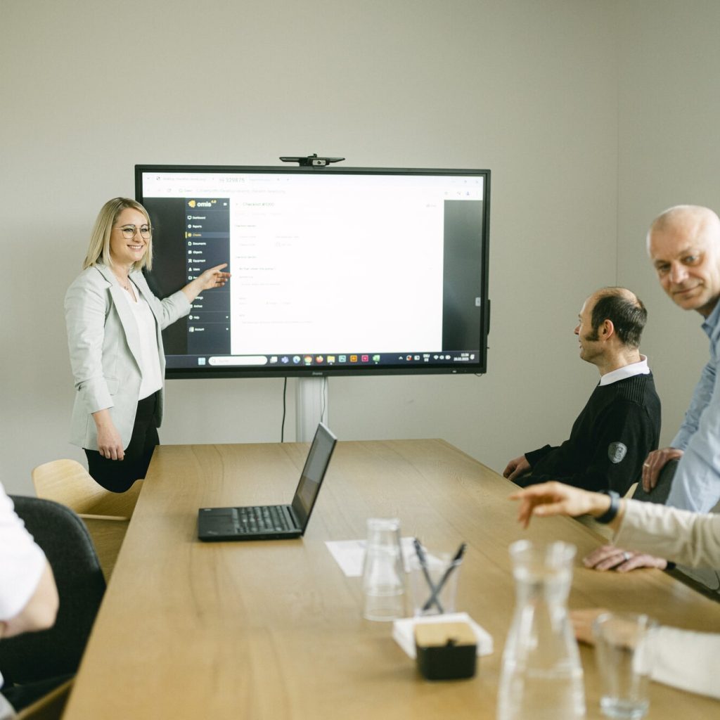 Präsentation am Bildschirm – Frau zeigt einem Team, wie die omis Software zur Berichtserstellung genutzt wird.