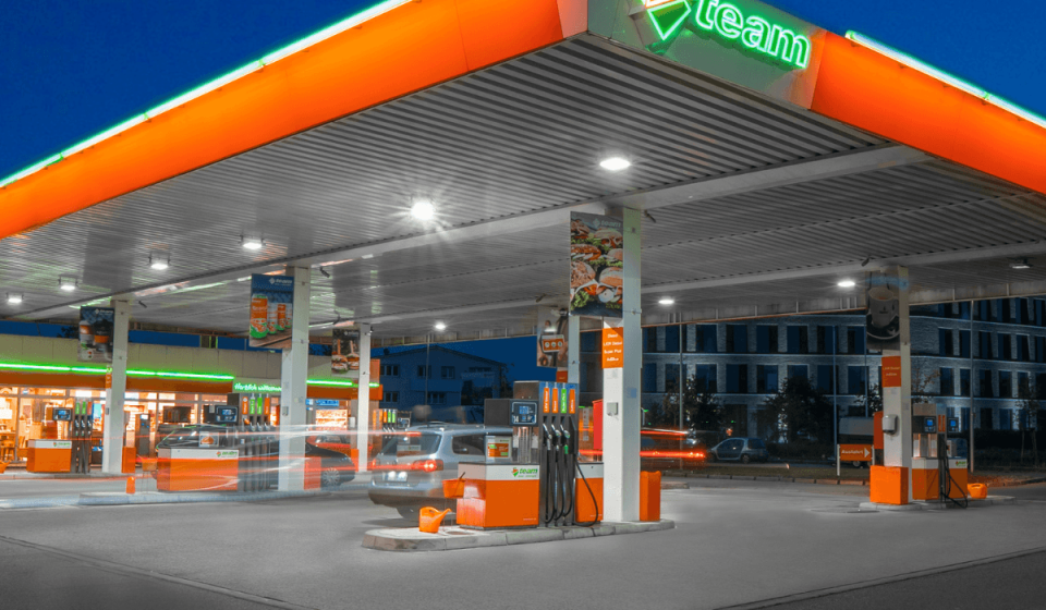 Beleuchtete TEAM-Tankstelle am Abend mit modernen Zapfsäulen, überdachter Fahrbahn und angeschlossenem Shop – Sinnbild für energieeffiziente Infrastruktur und kundenorientierten Service.
