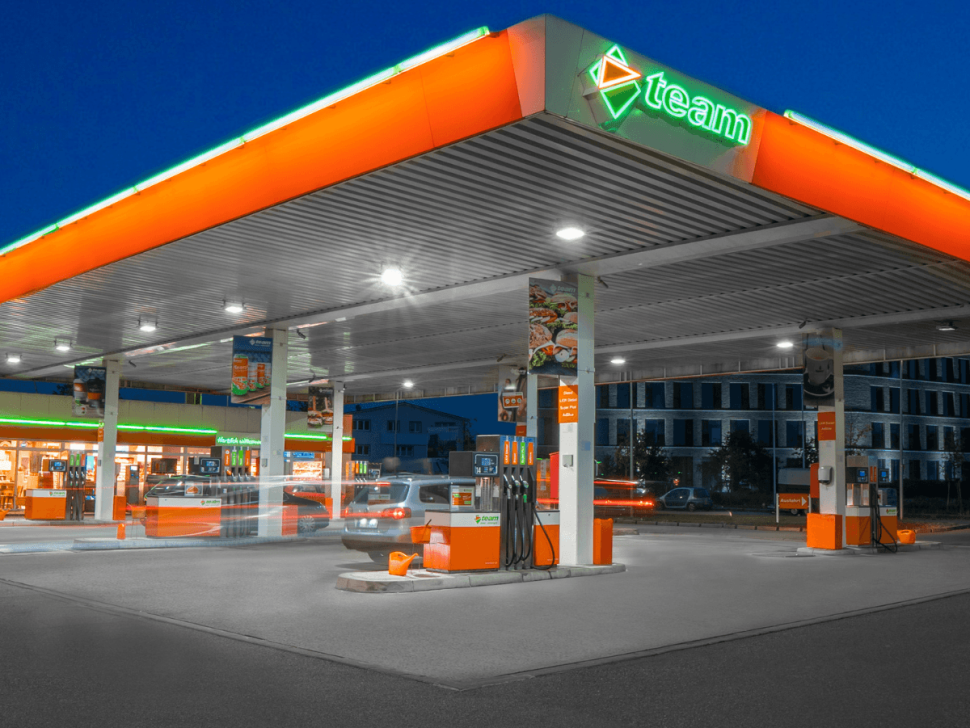 Beleuchtete TEAM-Tankstelle am Abend mit modernen Zapfsäulen, überdachter Fahrbahn und angeschlossenem Shop – Sinnbild für energieeffiziente Infrastruktur und kundenorientierten Service.